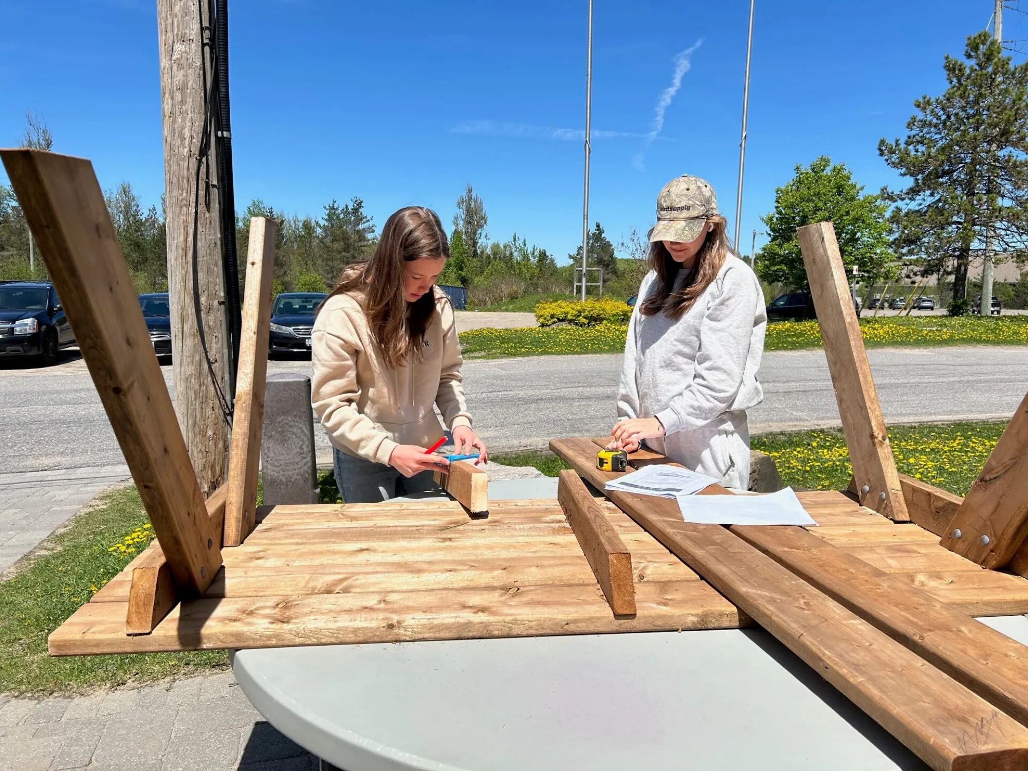 Two students measuring lumber while building a picnic table outdoors