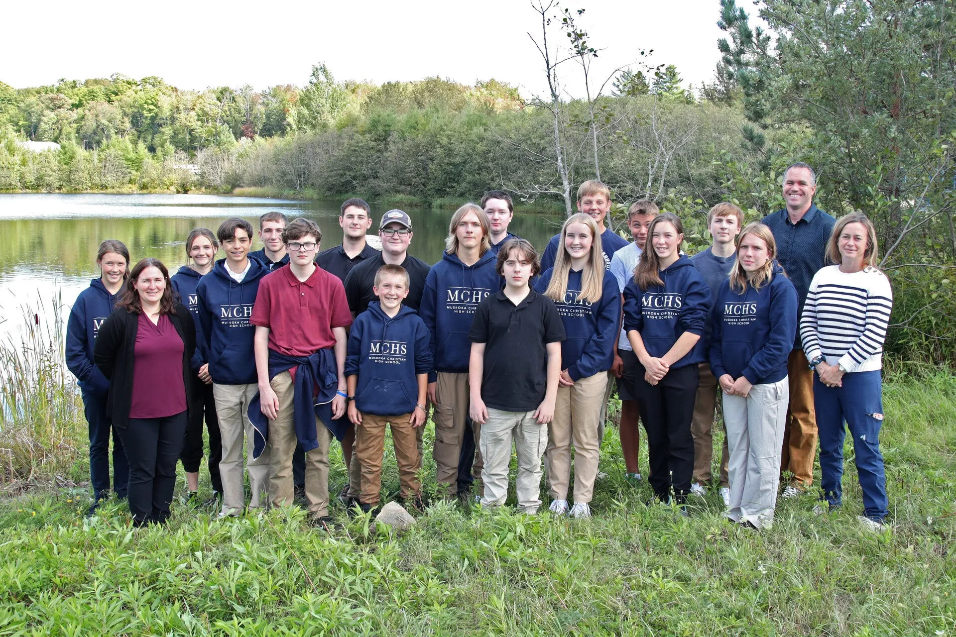 Muskoka Christian High School students in school sweaters gathered outdoors beside a lake