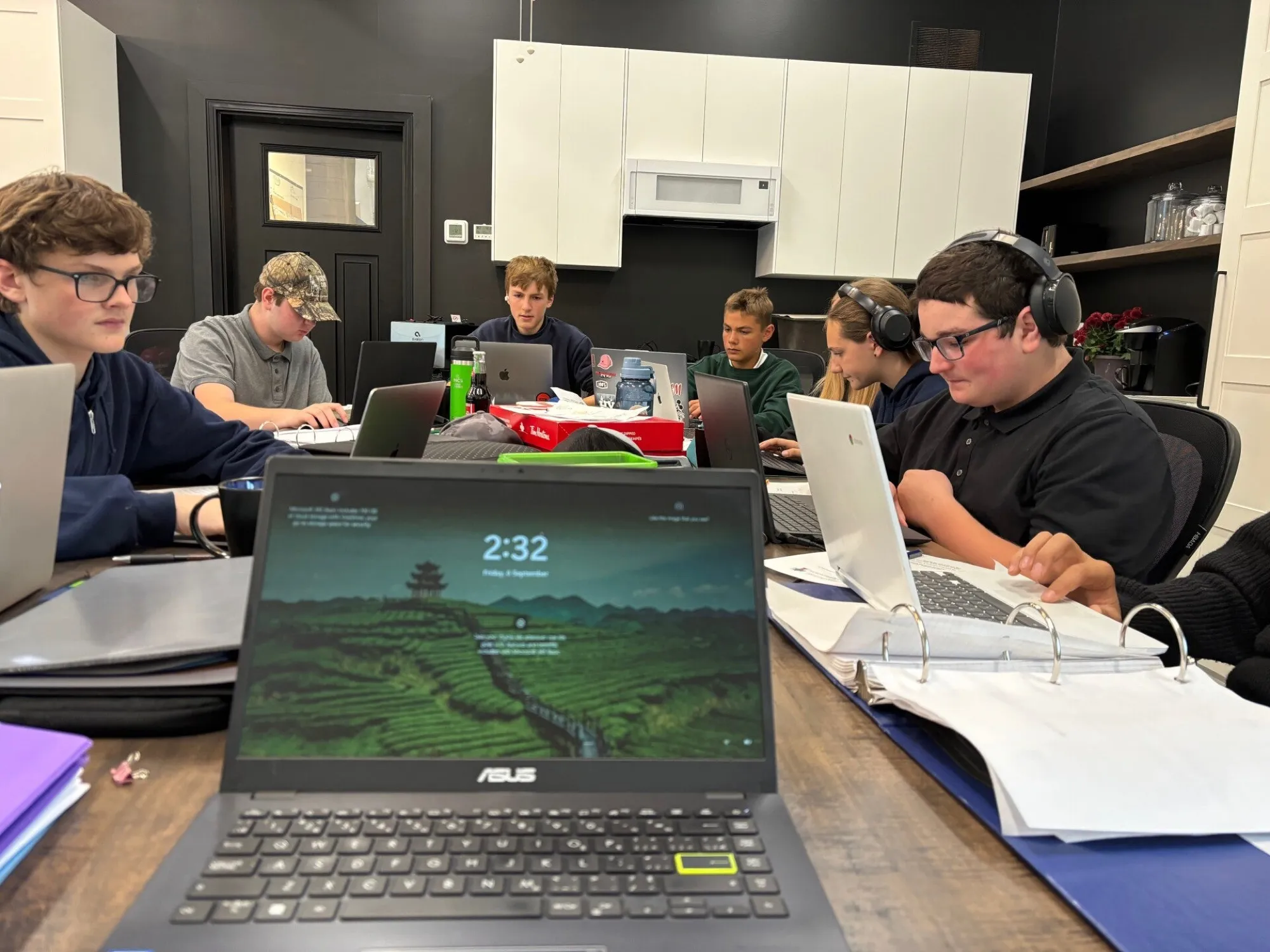 High school students working on laptops and notes around a classroom table